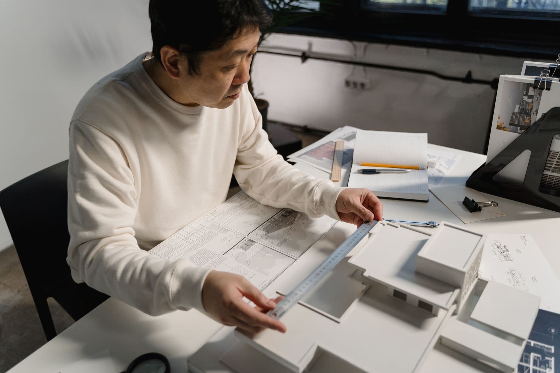 Architect measuring a scale model beside technical drawings