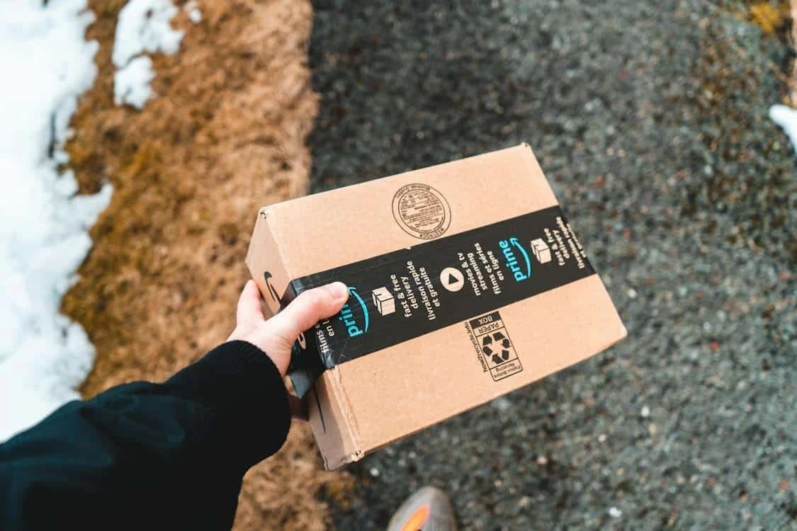 A hand holding a cardboard box with an Amazon logo.