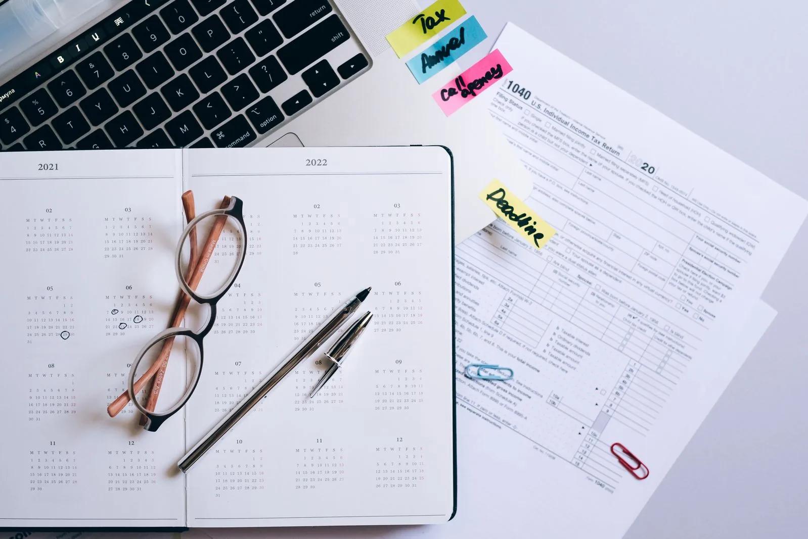Organised desk with a calendar planner, glasses and tax return documents for deadline filing