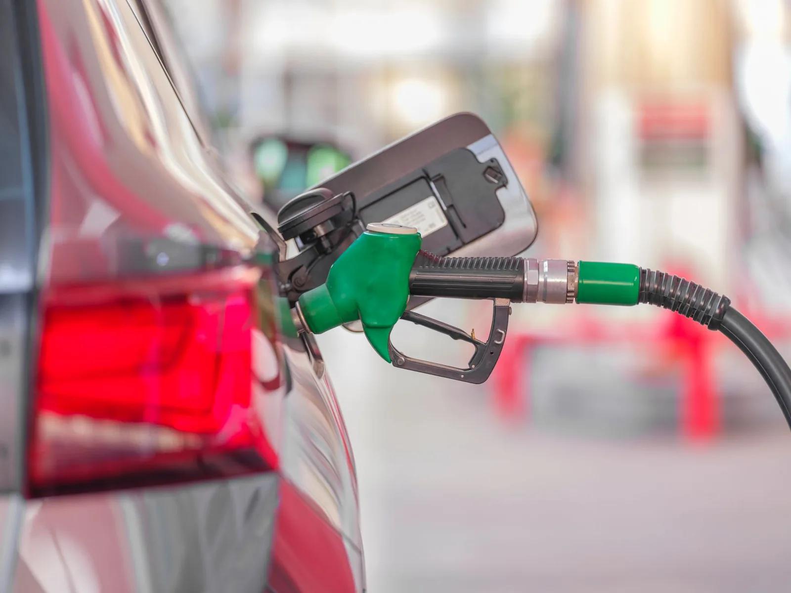 A green fuel pump nozzle inserted into a car's fuel tank at a UK petrol station forecourt in daylight