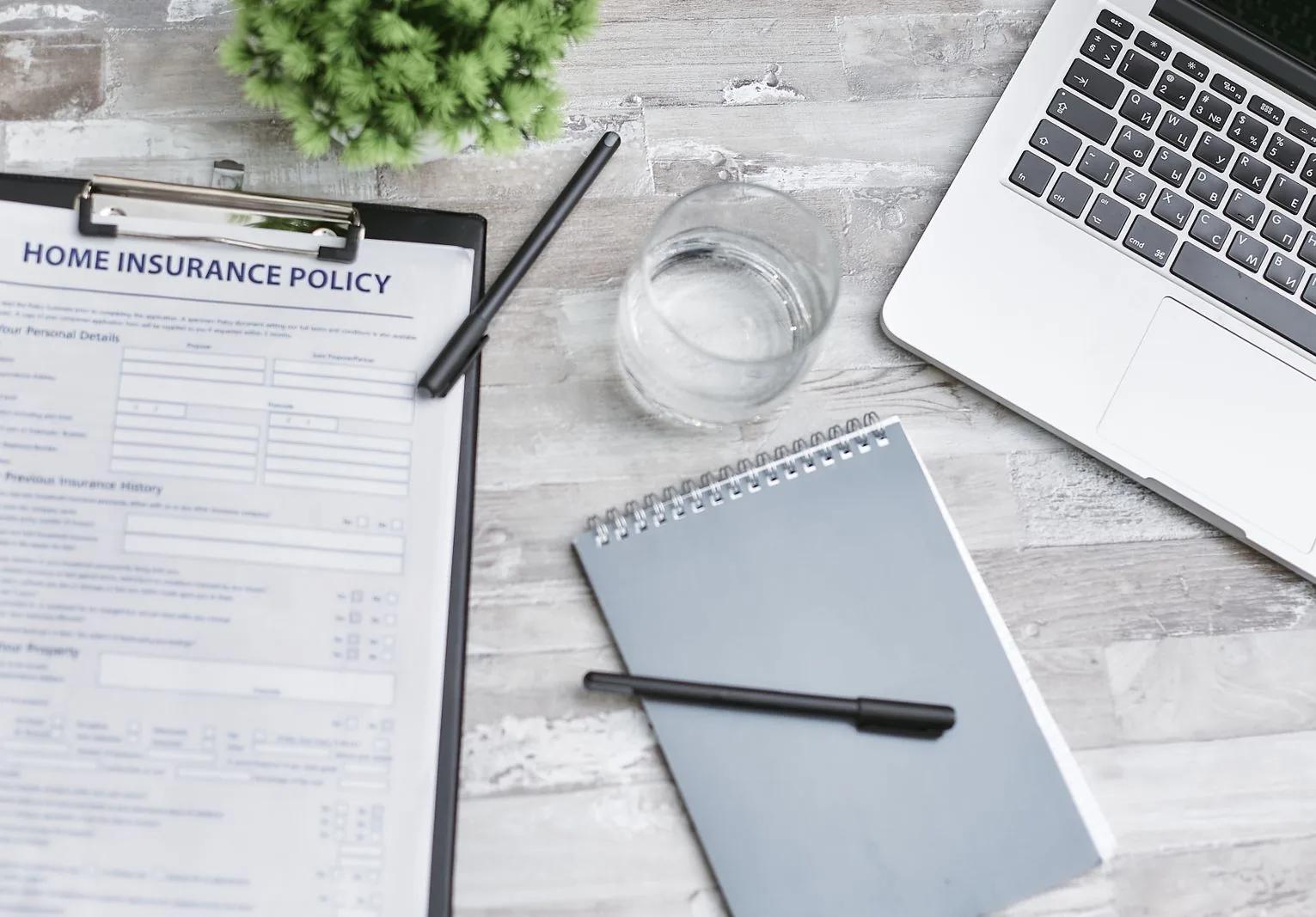 Landlord's desk flat-lay with home insurance policy, laptop and notebook for rental income paperwork