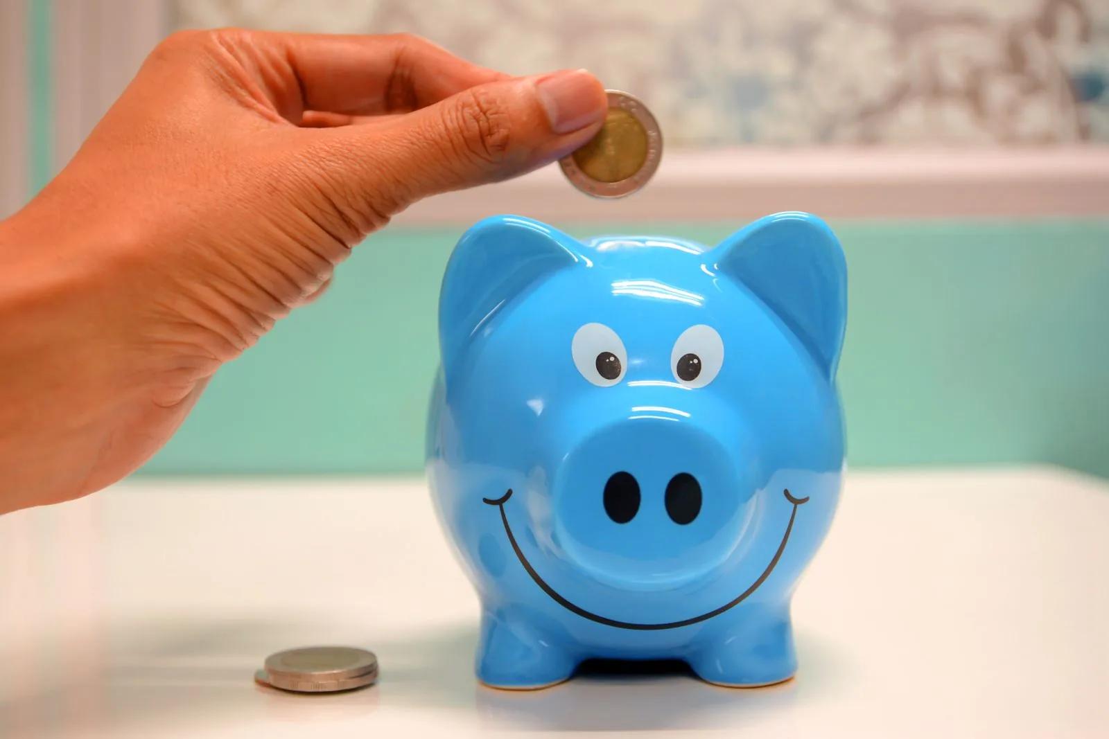 Hand dropping a coin into a blue piggy bank symbolising long-term savings