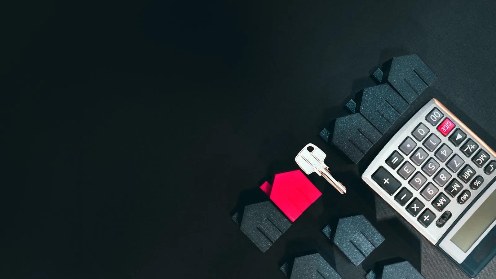 Calculator, model houses and a key on a dark surface symbolising property finance