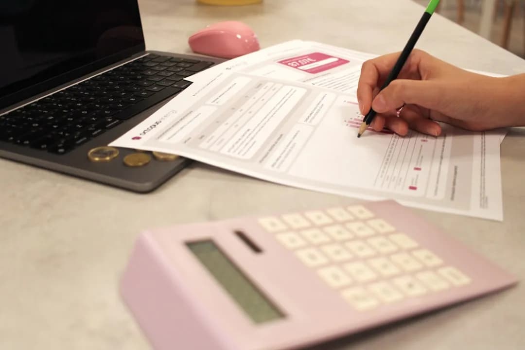 A childminder at a kitchen table logging income and expenses in a simple bookkeeping notebook