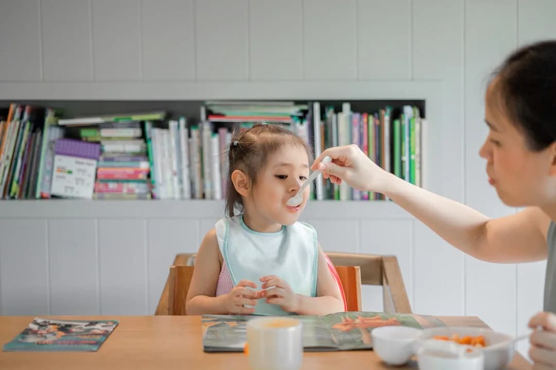 A childminder preparing a healthy lunch for toddlers at a kitchen table in a home setting