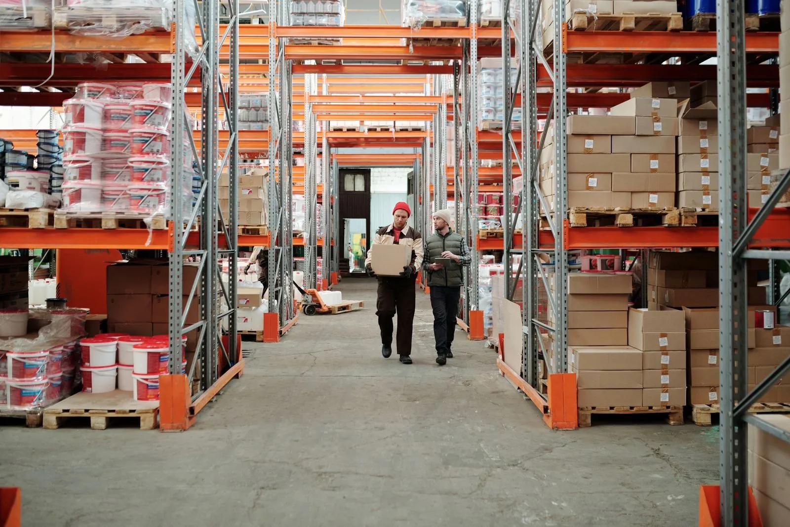 Warehouse workers handling a package among shelves stocked with boxes and inventory