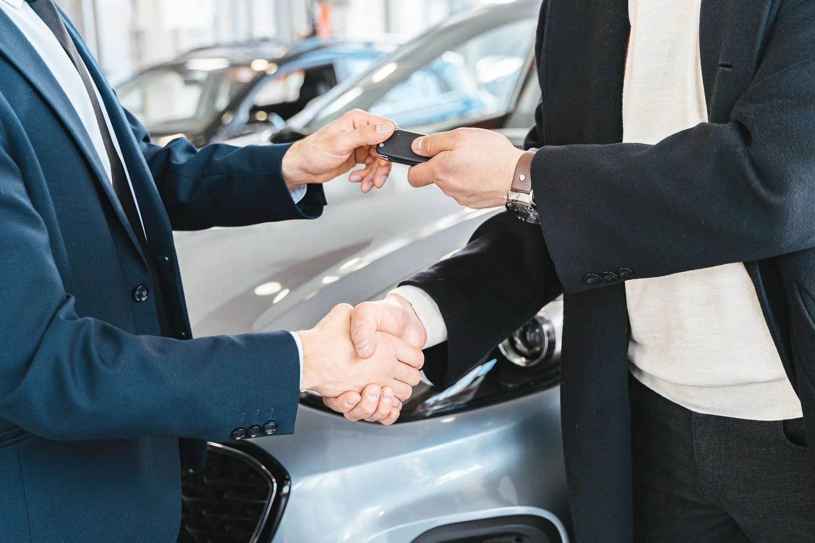 Two businessmen shaking hands and exchanging car keys at a dealership