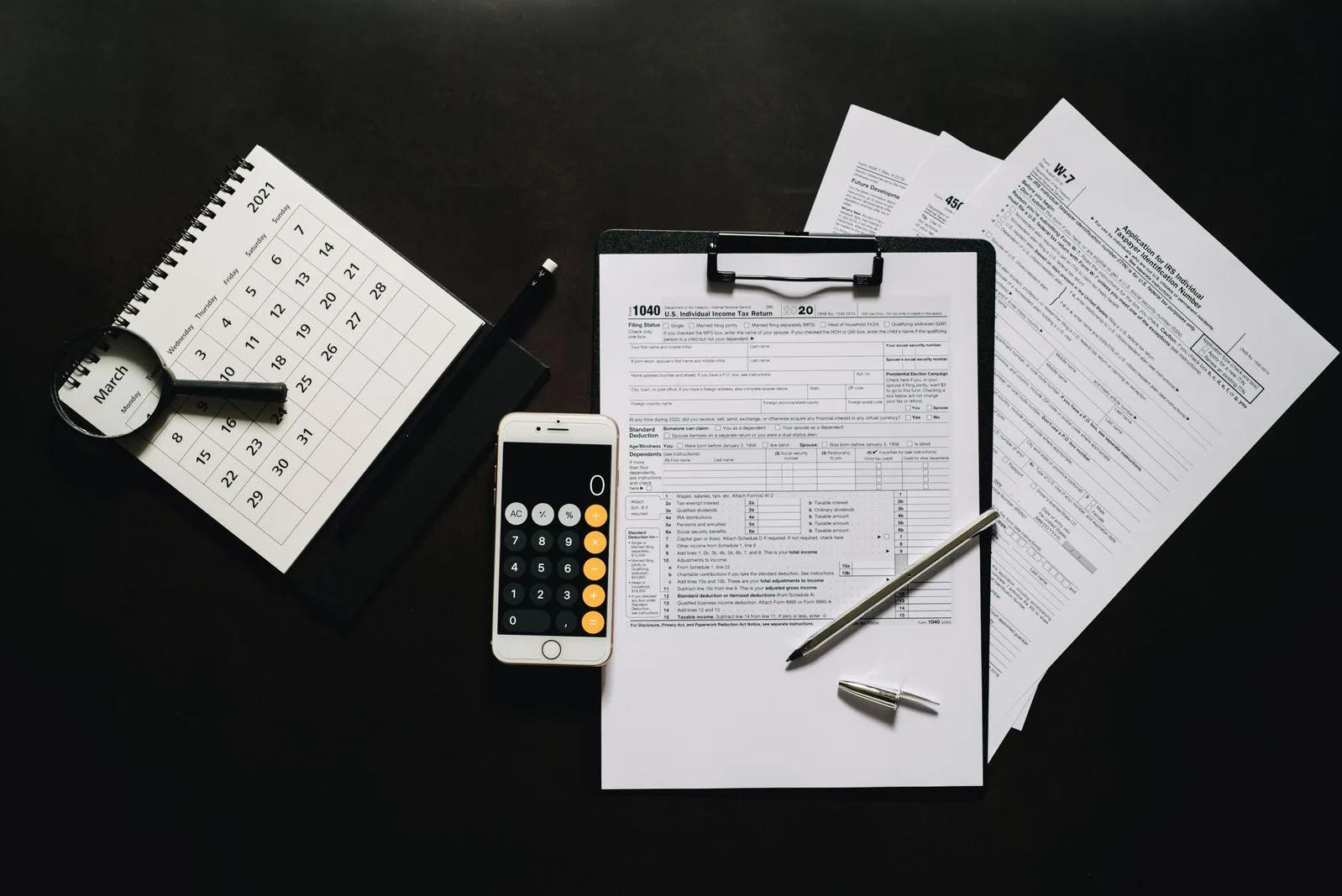 Flat lay of company tax return forms, calculator, calendar and pen on a desk