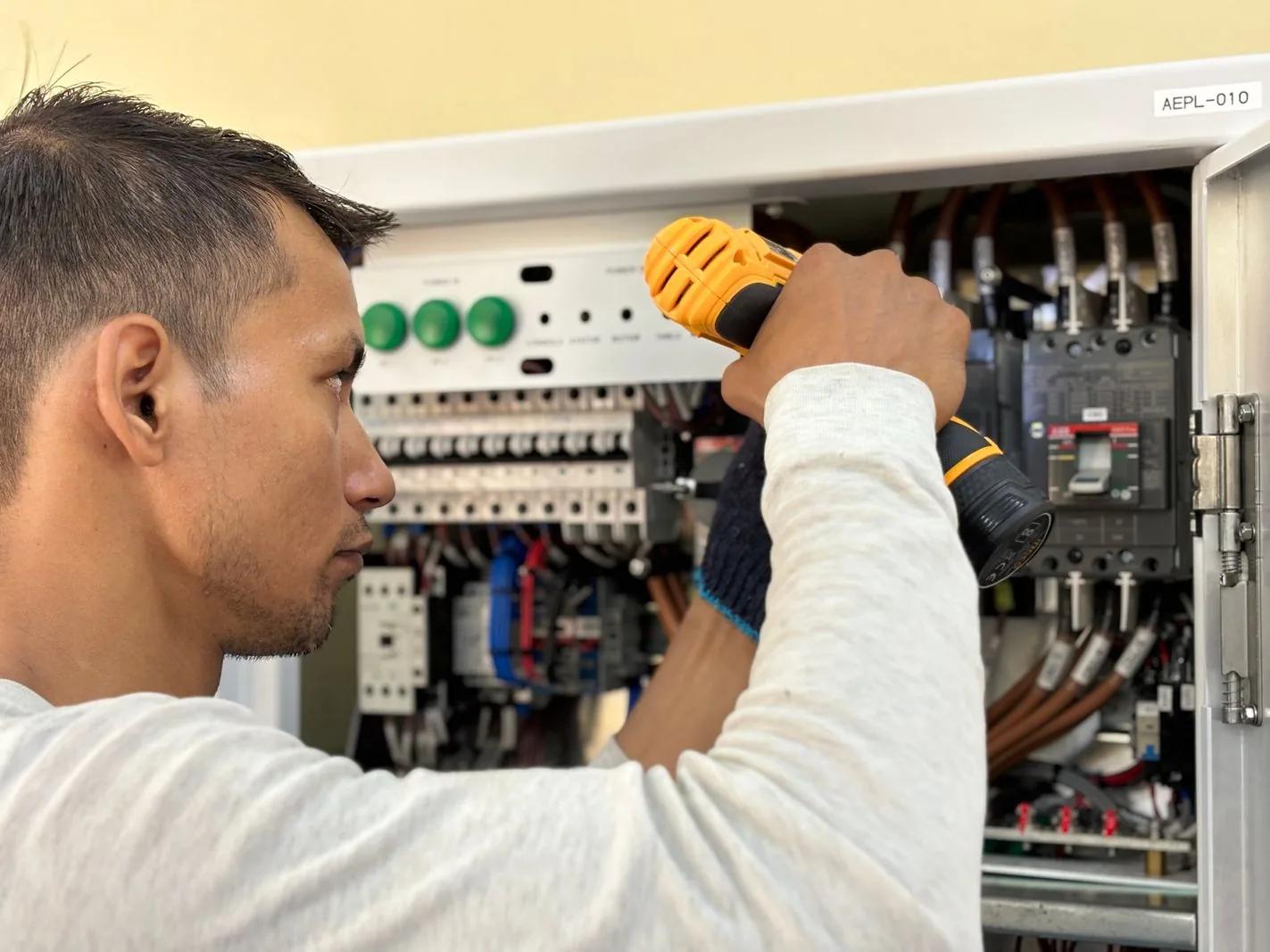 Professional electrician using a drill on an indoor consumer unit circuit breaker panel