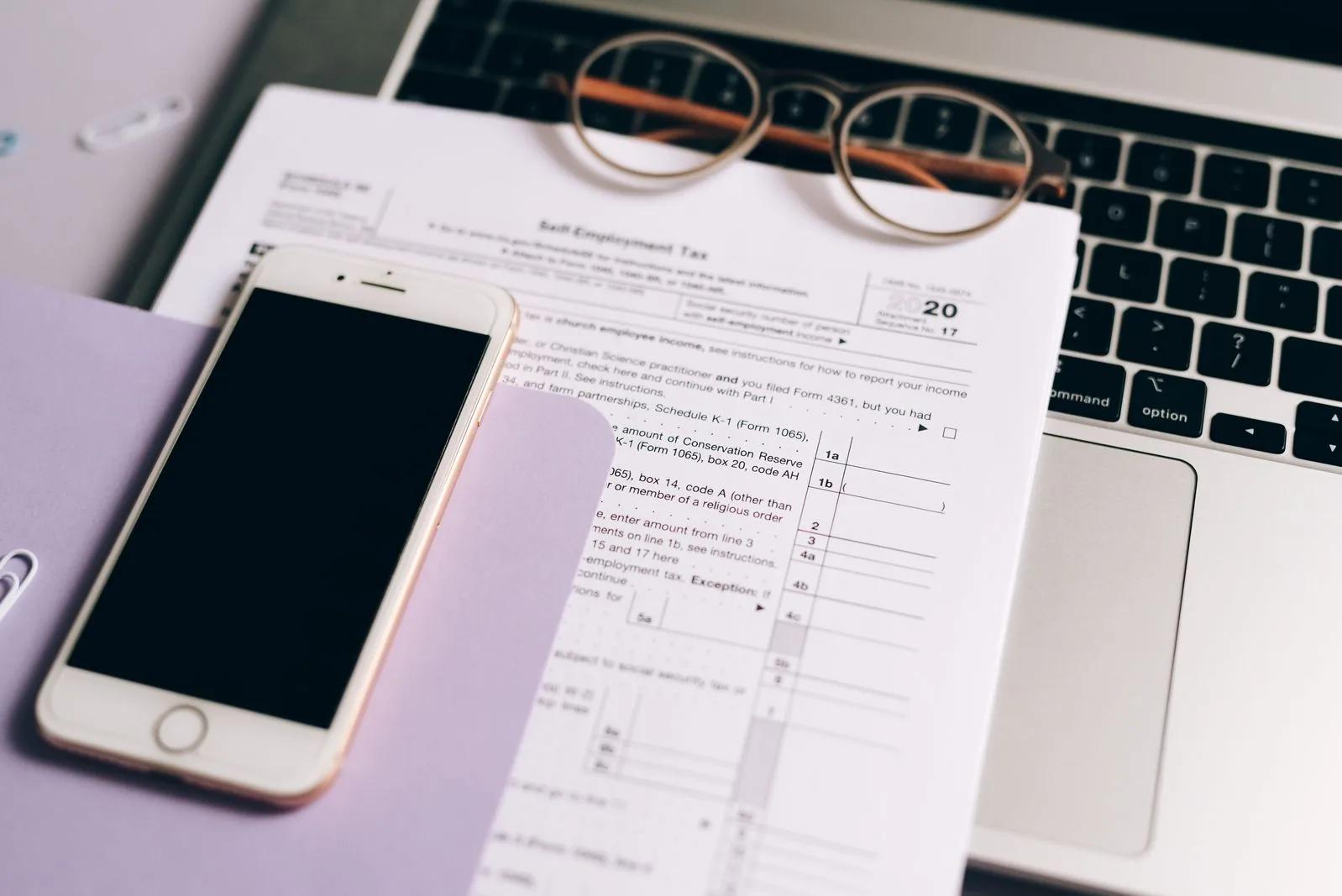 Close-up of self assessment tax documents beside a laptop and smartphone on a desk