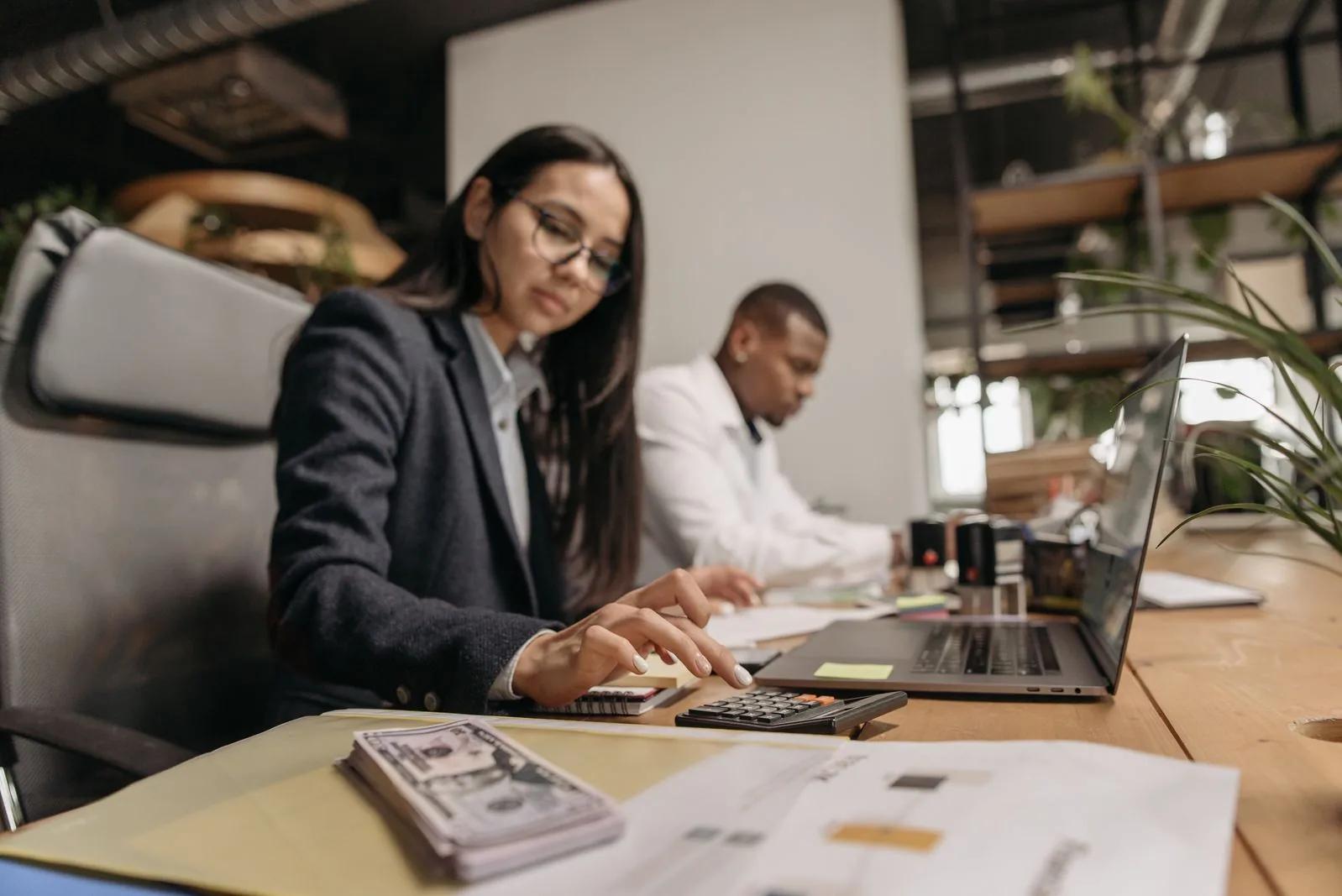 Two business professionals discussing accounts with a laptop and calculator in an office
