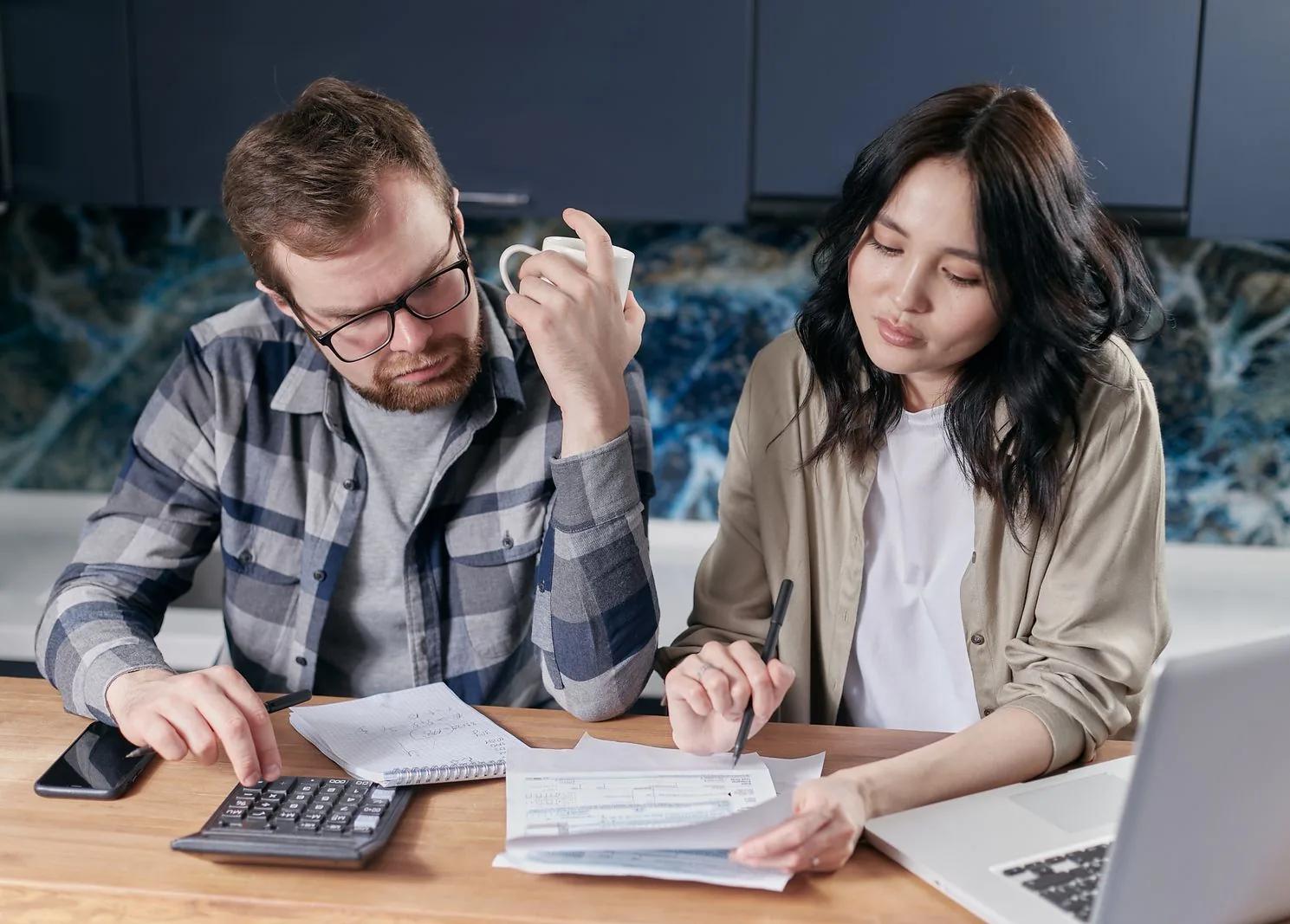 A couple reviewing household finances together with a laptop and calculator at their kitchen table