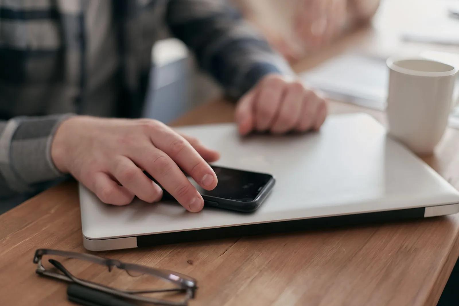 A UK small business owner signing in to an online government service on a laptop and smartphone at a bright, tidy home-office desk