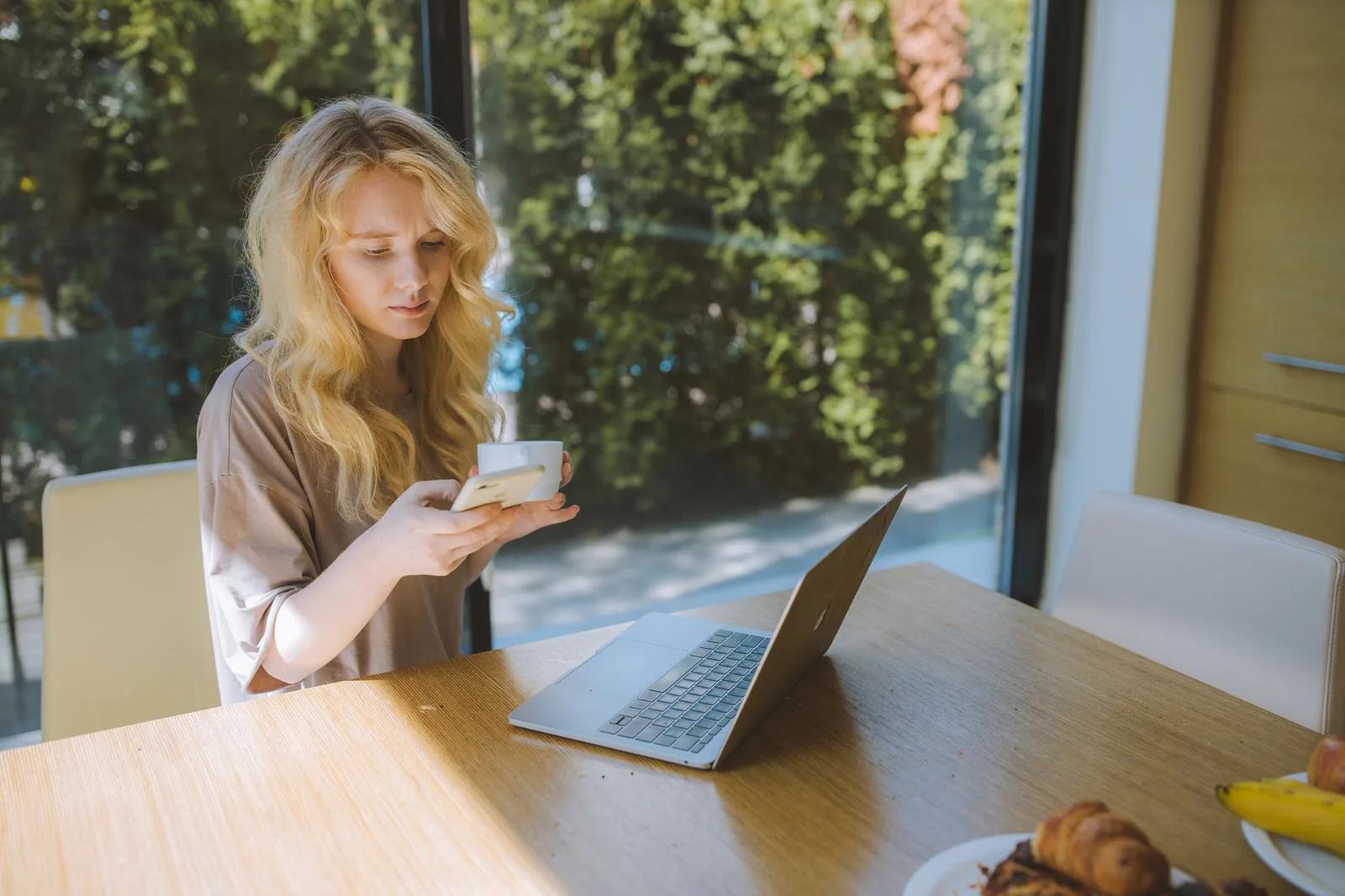 A small business owner signing in to HMRC online services on a laptop while a one-time access code arrives on a mobile phone