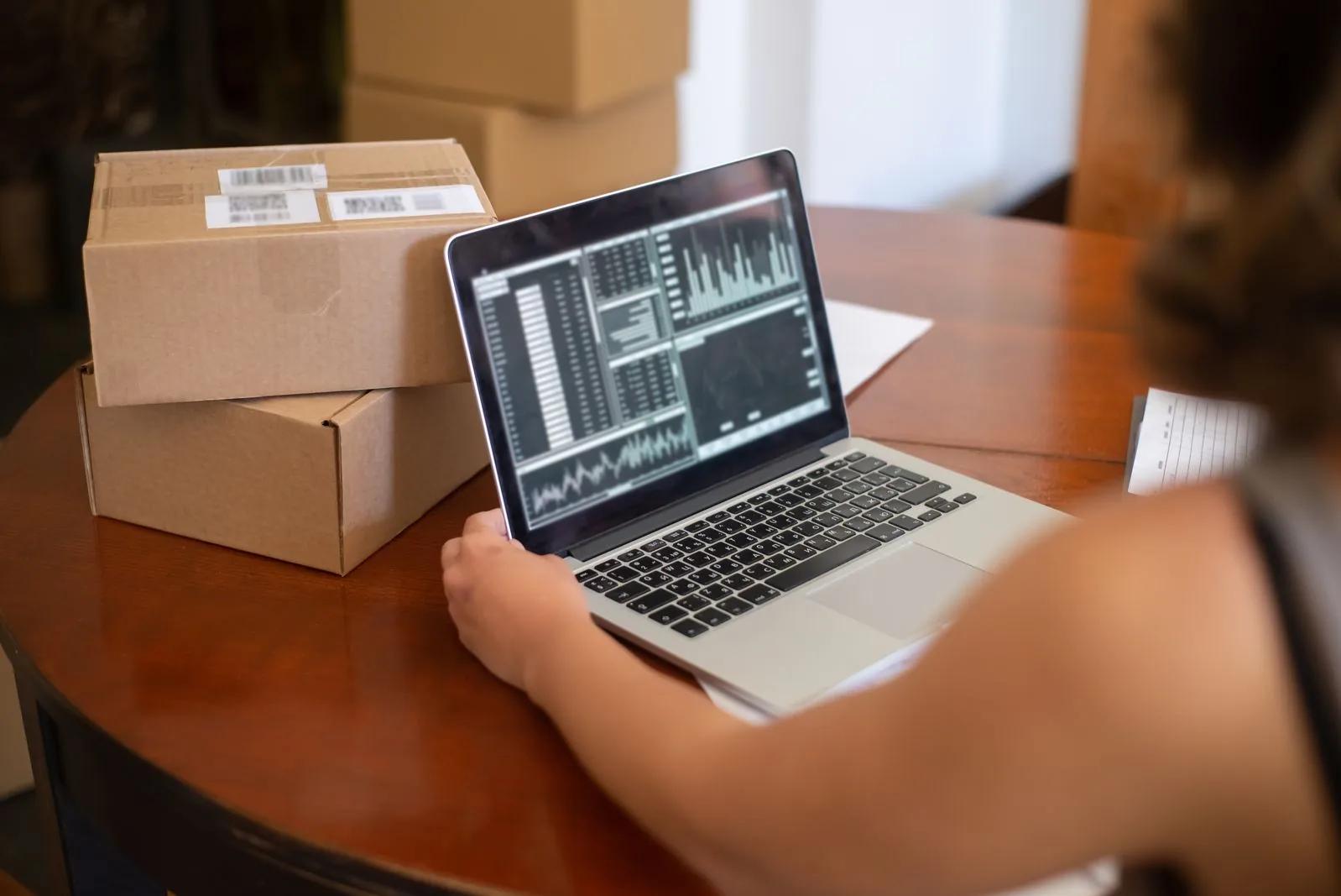 Online marketplace seller reviewing sales data on a laptop beside a shipping parcel