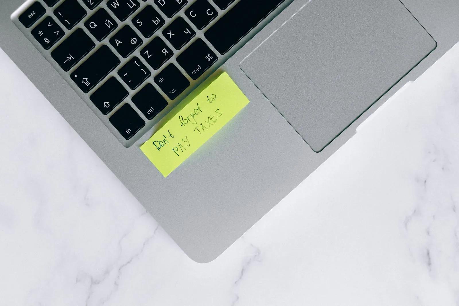 Laptop on a desk with a yellow sticky-note tax reminder