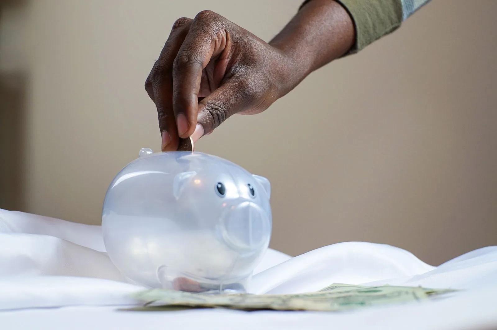A hand dropping a coin into a clear piggy bank, representing a sole trader setting money aside for a tax bill