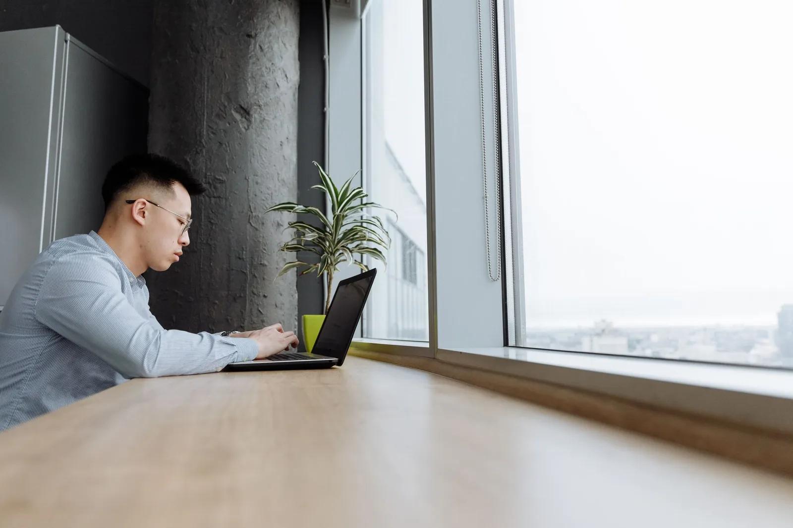 A UK small business owner working on a laptop at a bright desk by a window, organising their bookkeeping and digital records