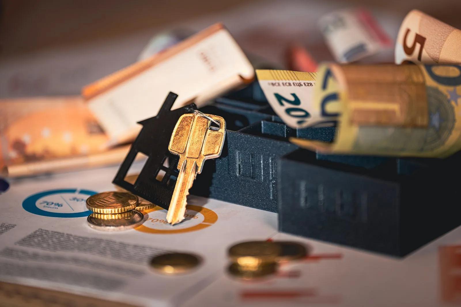 House key on a model house with banknotes and financial charts on a desk