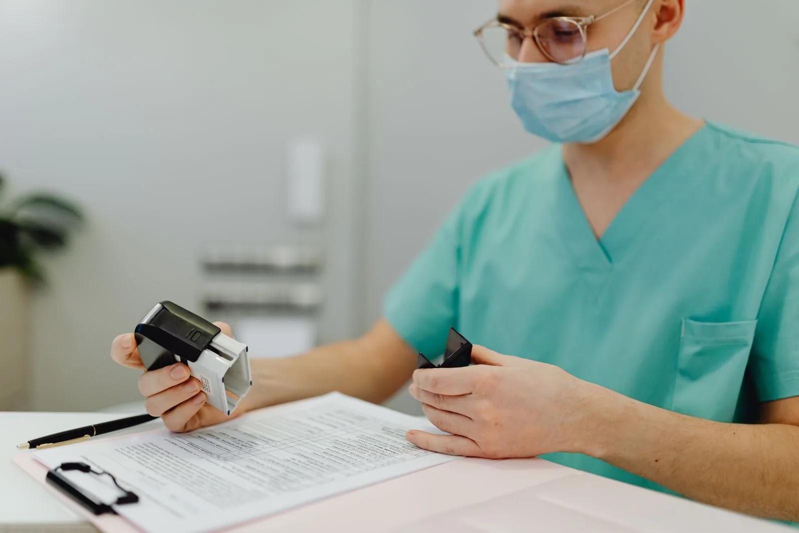 Healthcare professional in scrubs reviewing and stamping documents at a clinic desk