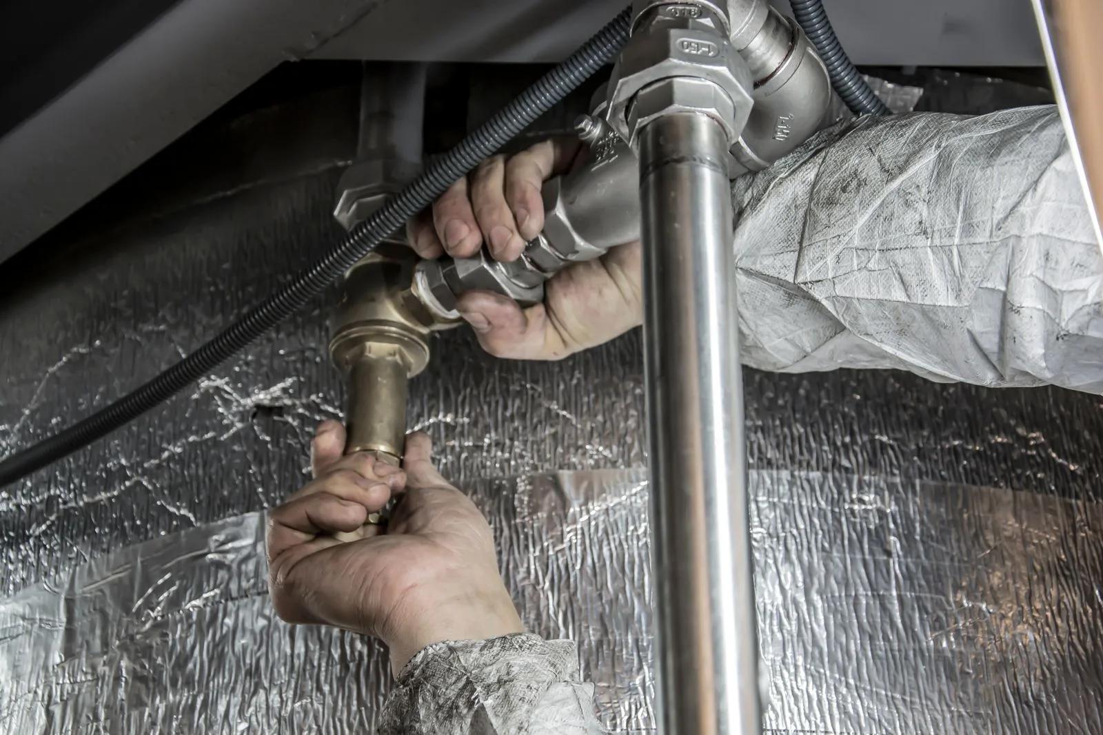 Close-up of a plumber's hands fitting steel and brass pipework under a unit