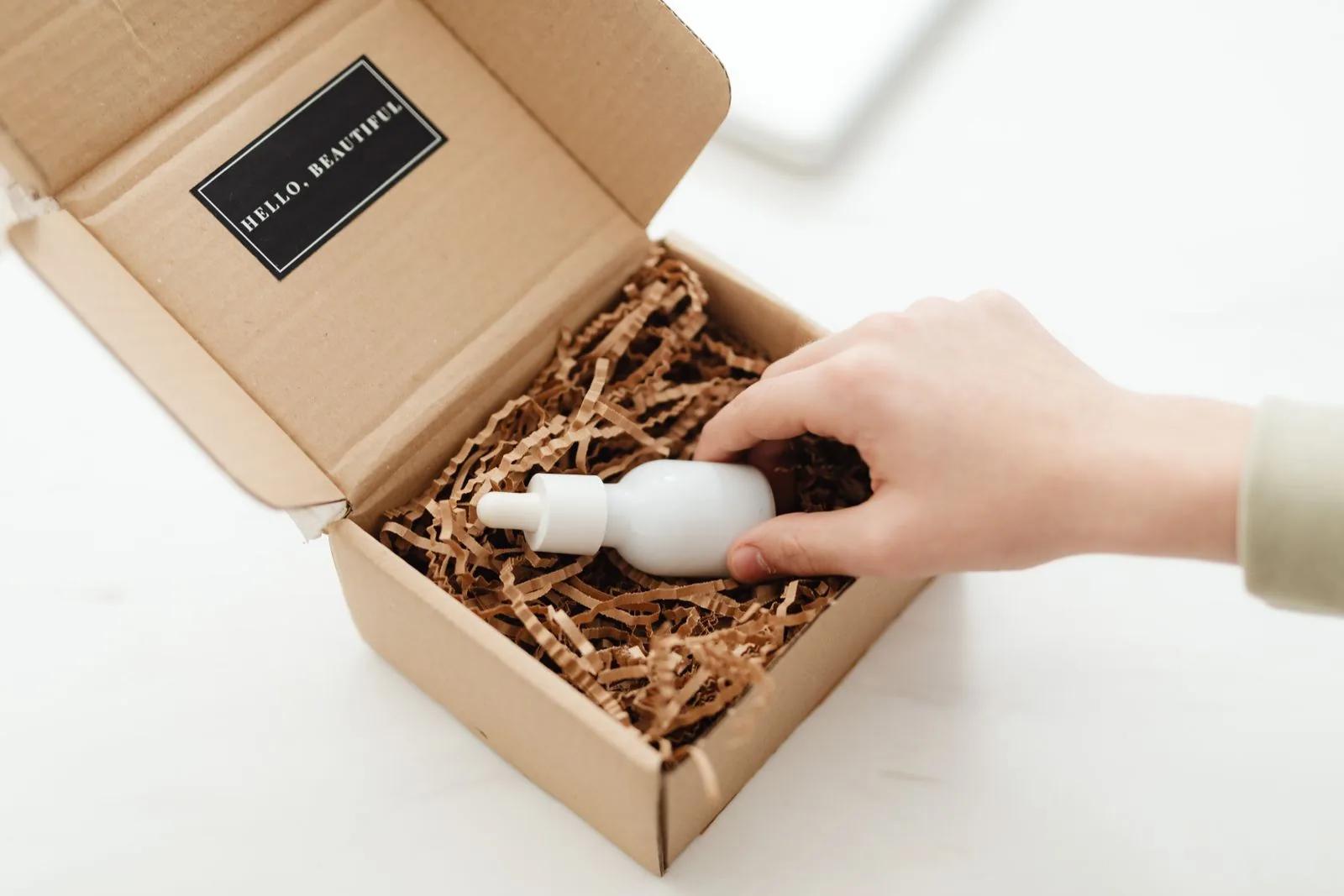 Hands unboxing a beauty PR gift from a cardboard package filled with shredded paper