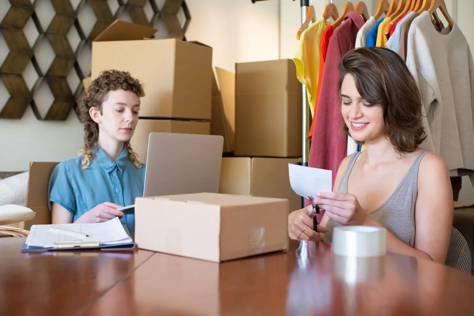 Two women managing an online clothing store with shipping boxes and a laptop