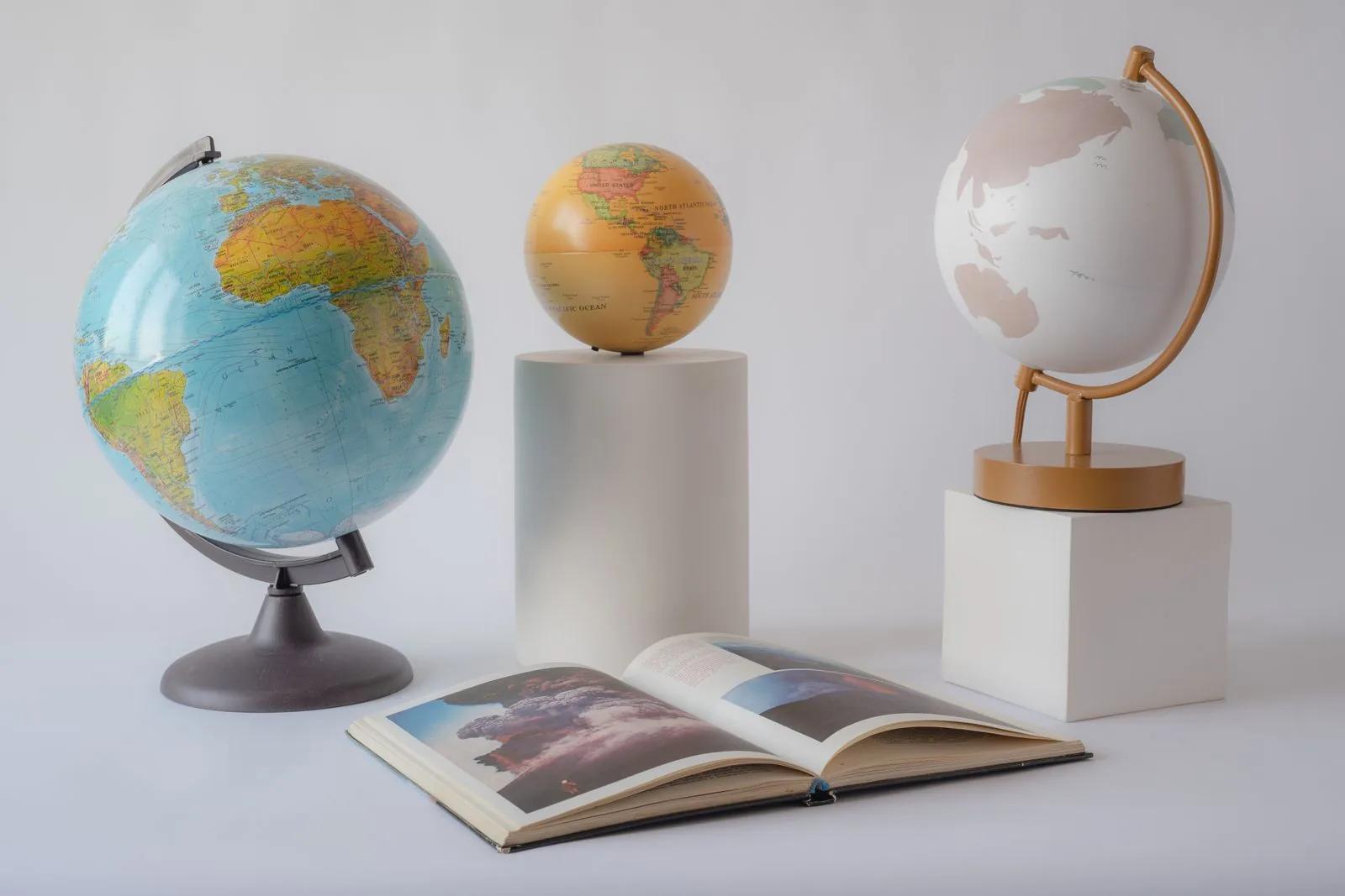 Three world globes and an open book arranged on a clean light background