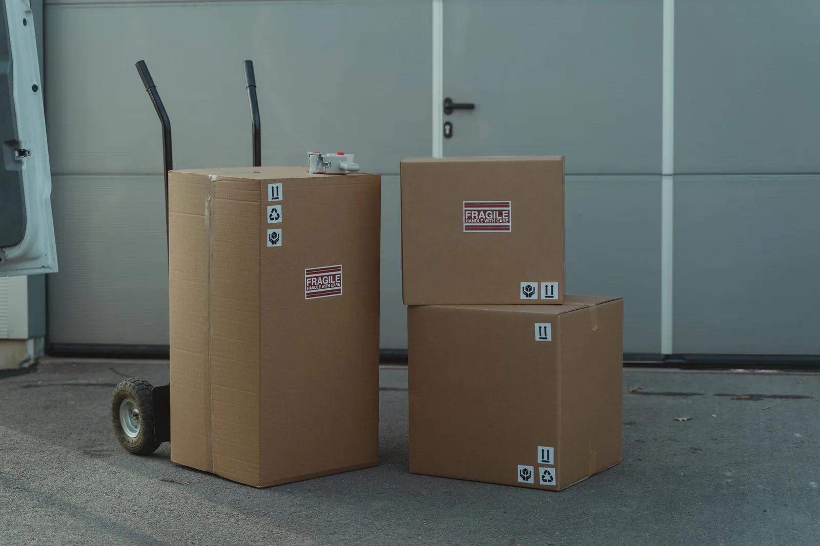 Cardboard shipping parcels stacked on a hand trolley beside a delivery van outside a warehouse