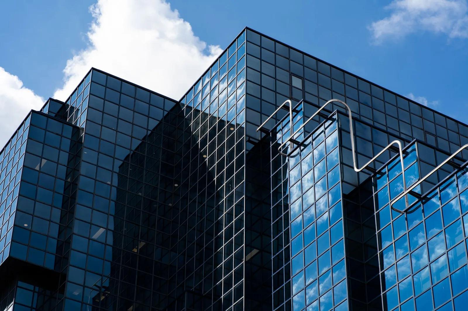 A modern glass-clad commercial office building photographed from below against a blue sky, representing a commercial property purchase assessed under the VAT Capital Goods Scheme thresholds