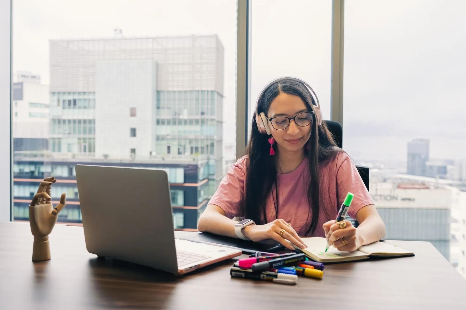 A UK small business owner making notes beside a laptop at a bright office desk while working on the company's year-end accounts