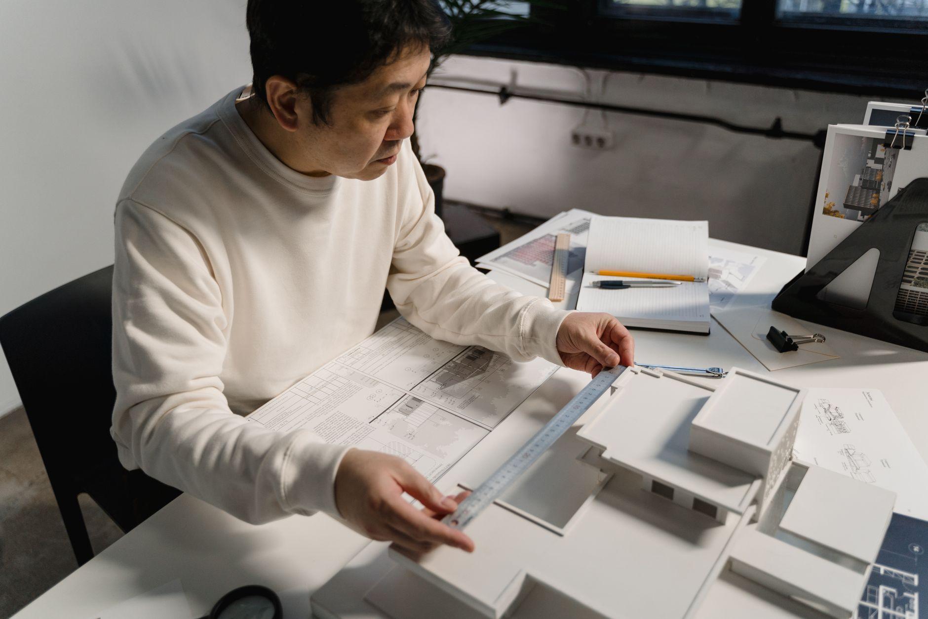 Architect measuring a scale model beside technical drawings