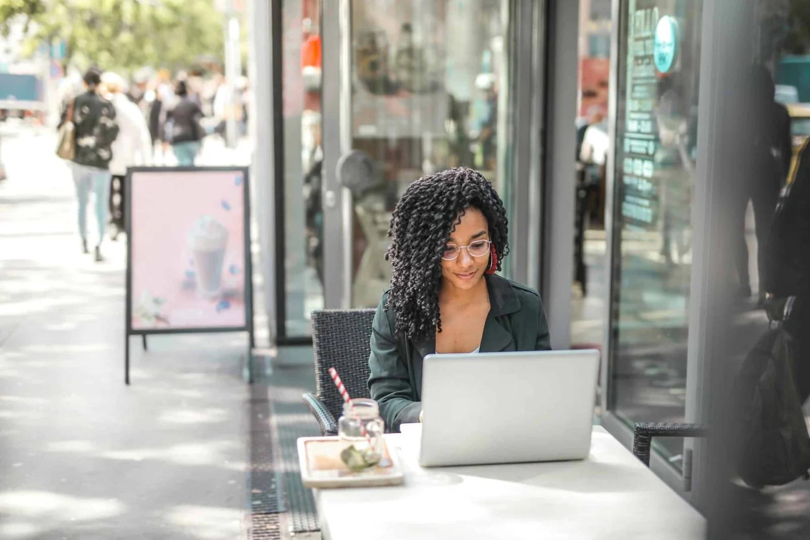 A woman working on a laptop in a cafe with paperwork spread out.
