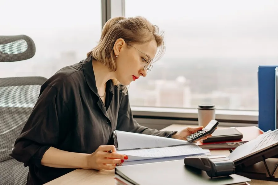 An accountant reviewing financial paperwork and checking the figures on a calculator at a bright city office desk An accountant reviewing financial paperwork and checking the figures on a calculator at a bright city office desk