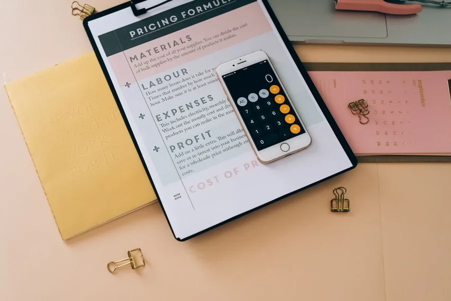 A small business pricing worksheet breaking down materials, labour, expenses and profit beside a phone calculator A small business pricing worksheet breaking down materials, labour, expenses and profit beside a phone calculator