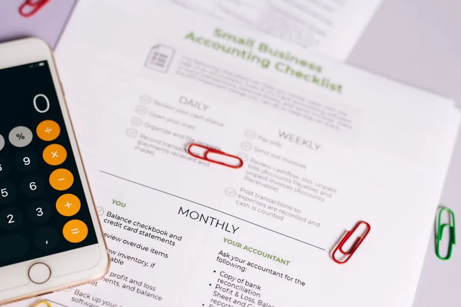 A small business accounting checklist flagging bills to pay and unpaid supplier invoices, next to a smartphone calculator