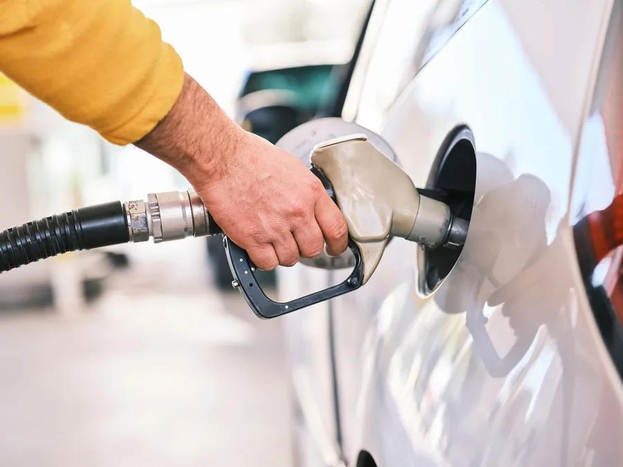 Grey fuel nozzle held in the filler neck of a clean white company car on a bright forecourt as the tank is topped up Grey fuel nozzle held in the filler neck of a clean white company car on a bright forecourt as the tank is topped up