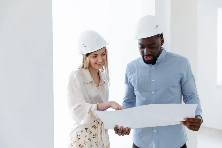 A contractor and client in hard hats reviewing building plans on site, the kind of subcontractor arrangement CIS gross payment status supports A contractor and client in hard hats reviewing building plans on site, the kind of subcontractor arrangement CIS gross payment status supports