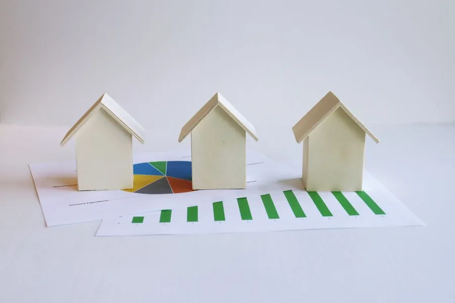 Wooden model houses arranged on printed bar charts and graphs, illustrating UK house price forecasts and market data
