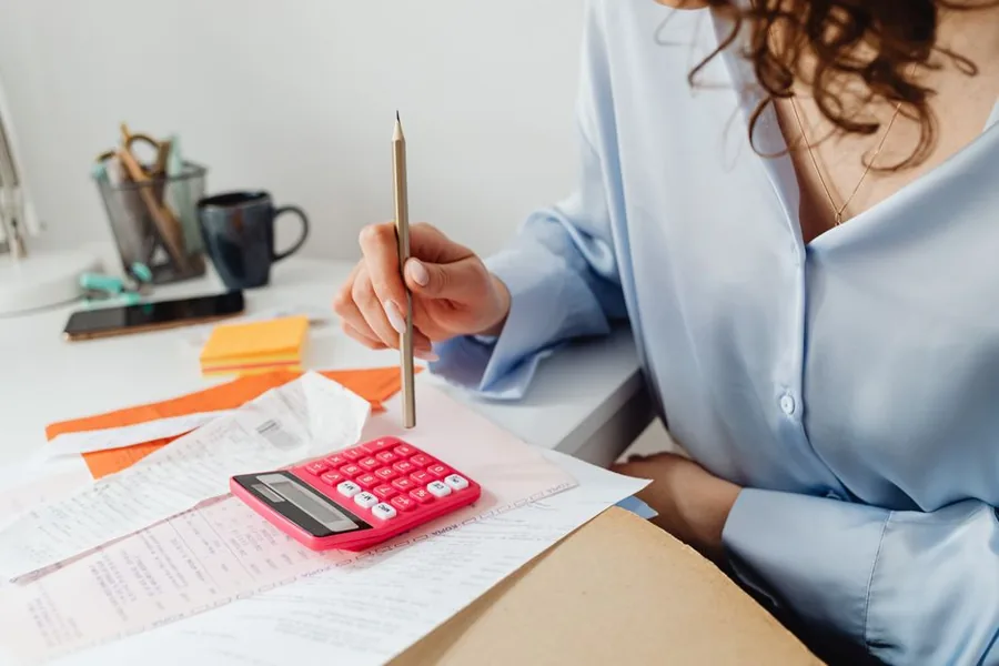 A small business owner checking paper receipts against her figures with a calculator while reconciling the accounts