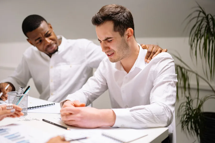 A manager offering emotional support with a hand on the shoulder of a colleague at a workplace desk