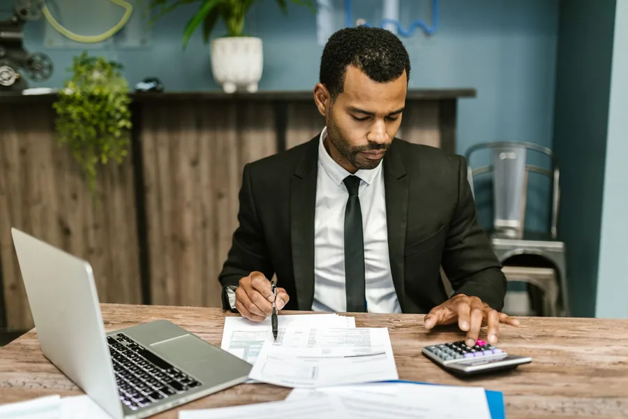 Small business owner reviewing accounts on an open laptop with paperwork and a calculator at a modern desk Small business owner reviewing accounts on an open laptop with paperwork and a calculator at a modern desk