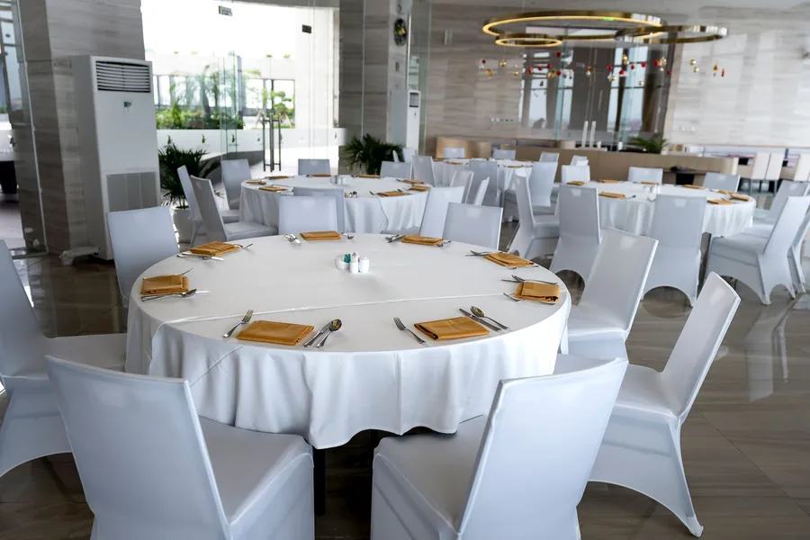 Round tables laid with white linen and napkins in a bright, empty hotel dining room ready for service Round tables laid with white linen and napkins in a bright, empty hotel dining room ready for service