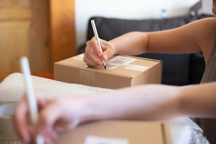An online marketplace seller checking order paperwork at a home packing station stacked with parcels ready to ship An online marketplace seller checking order paperwork at a home packing station stacked with parcels ready to ship
