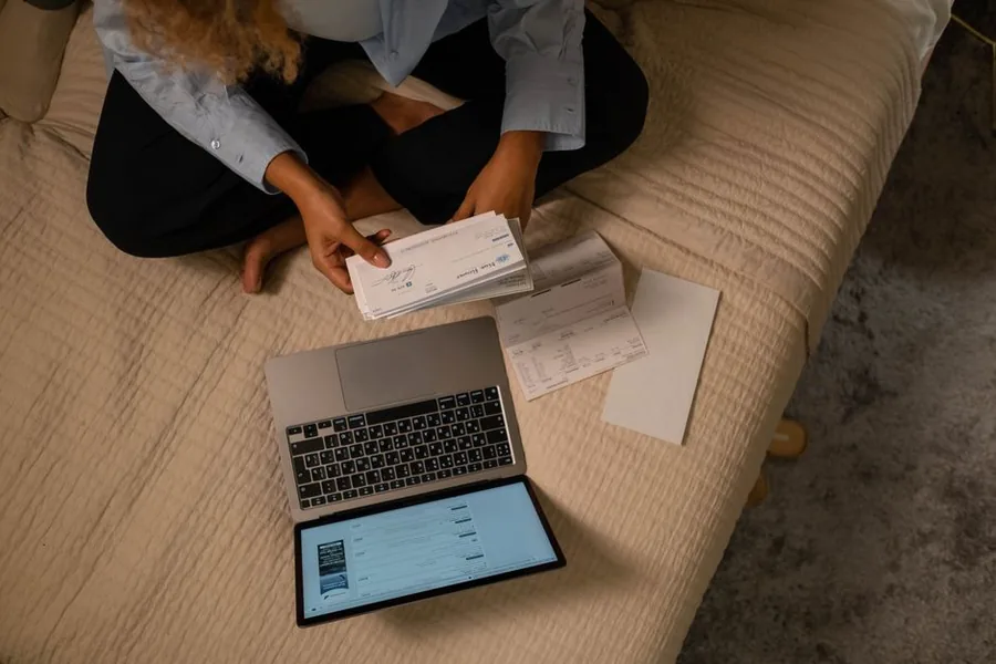 Someone at home reviewing bank statements and payments on a laptop while sorting through their financial paperwork Someone at home reviewing bank statements and payments on a laptop while sorting through their financial paperwork