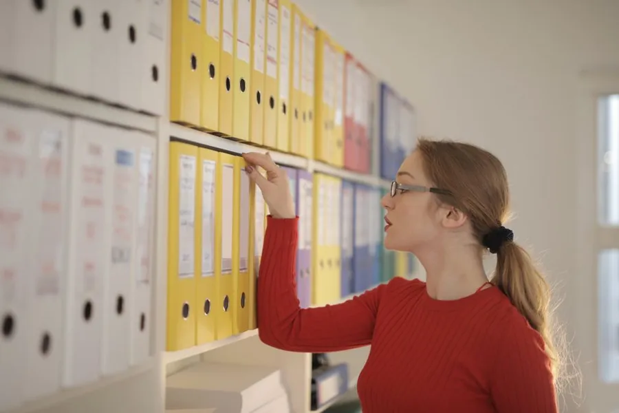 A sole trader sorting through labelled lever-arch files while organising her business records A sole trader sorting through labelled lever-arch files while organising her business records