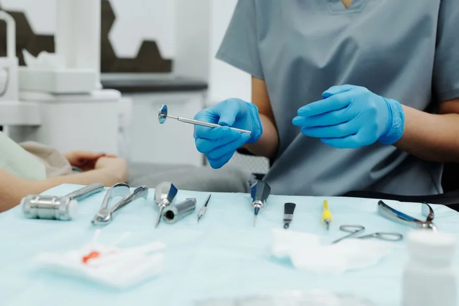 A dental associate in scrubs and blue gloves preparing instruments before treating a patient at a UK practice A dental associate in scrubs and blue gloves preparing instruments before treating a patient at a UK practice
