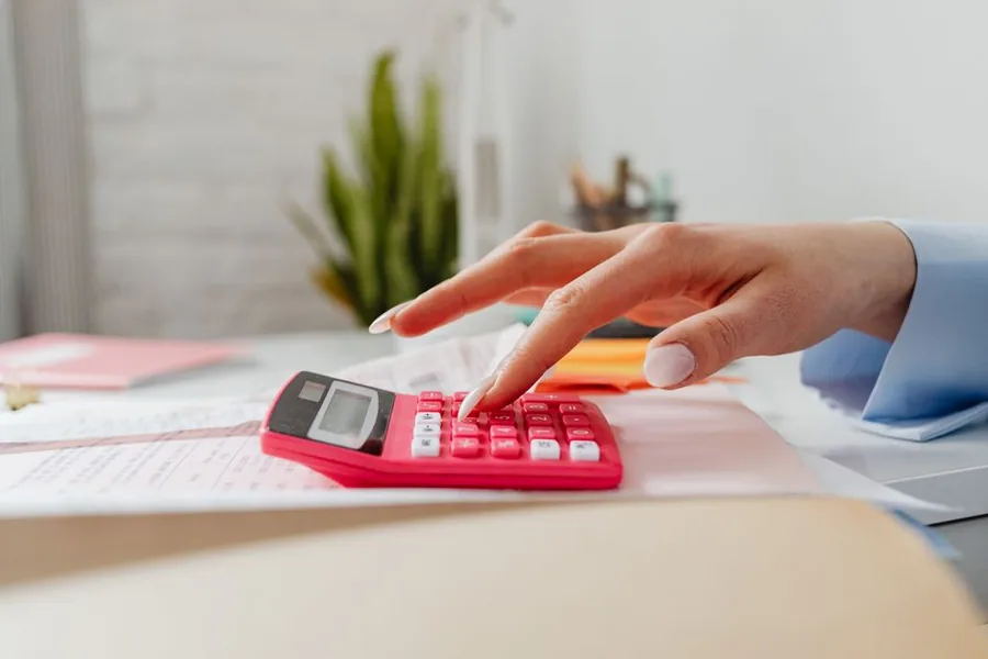 A childminder totting up daily expenses on a calculator while working through her bookkeeping paperwork