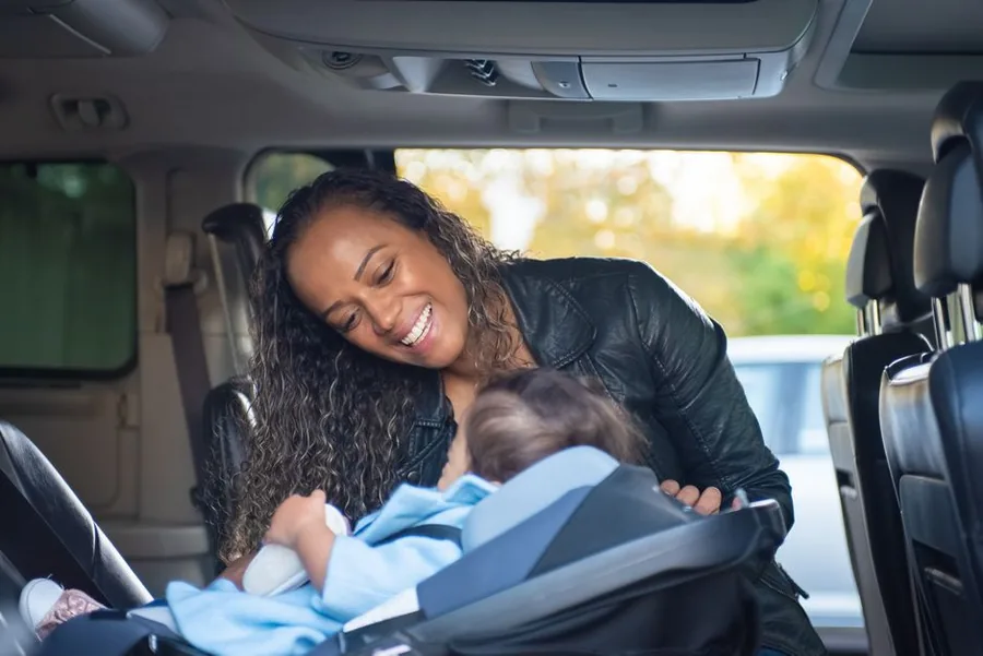 A childminder securing a young child into a car seat before a school run, the kind of journey that adds up to claimable mileage.