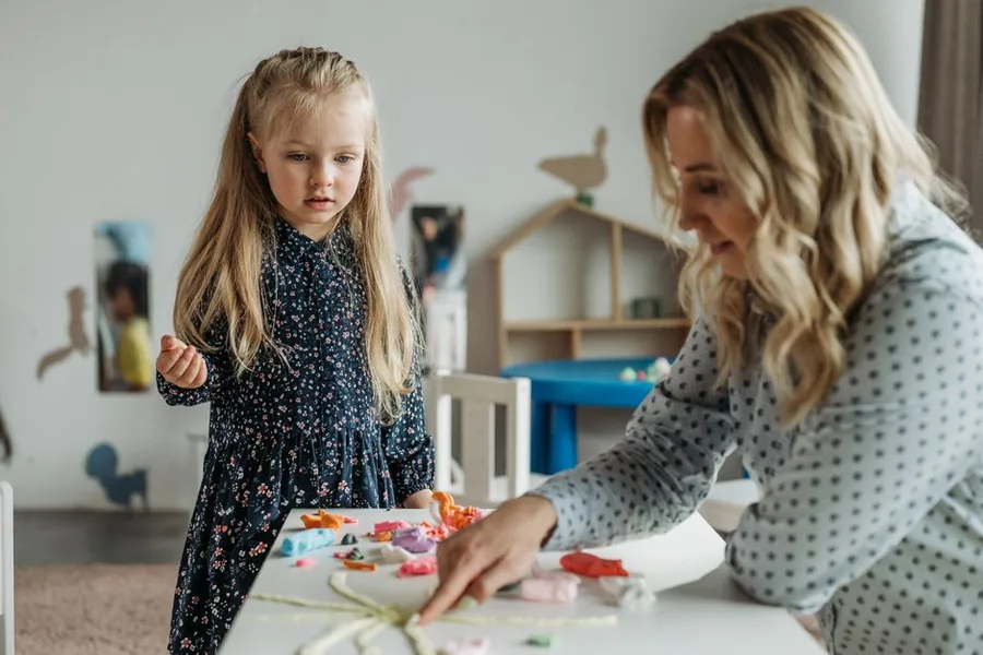 A childminder overseeing a group of young children at craft time, the workload that often prompts taking on an assistant A childminder overseeing a group of young children at craft time, the workload that often prompts taking on an assistant